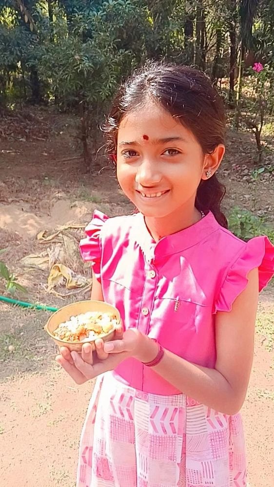 A smiling girl holding a bowl of prasad