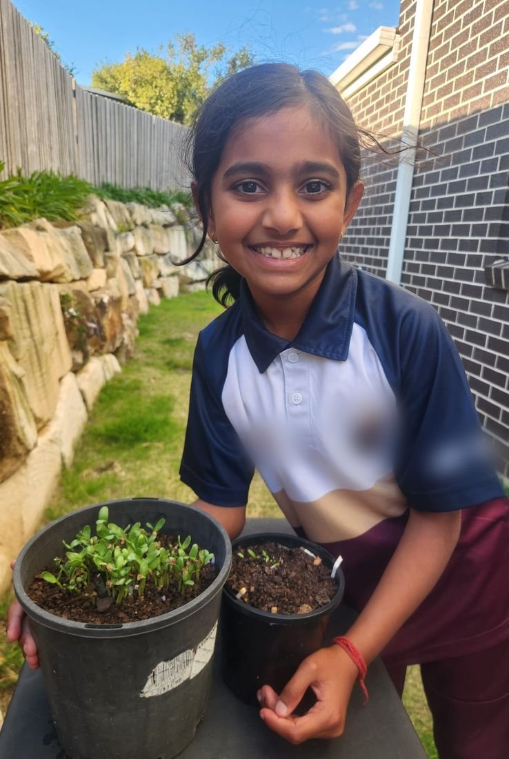 A girl beaming beside the seedlings she grew